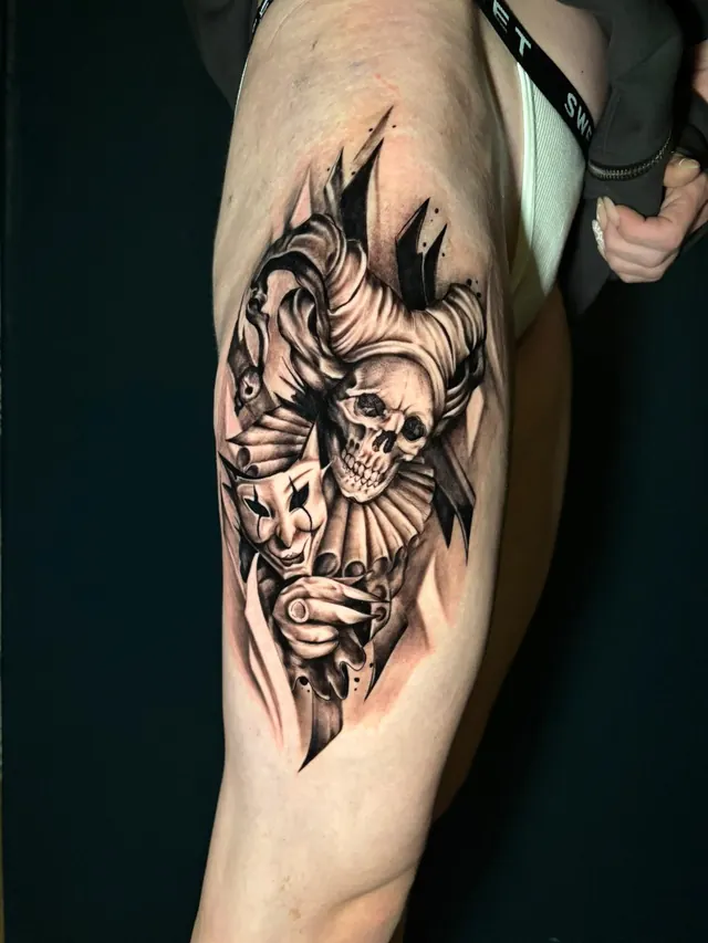 Black and grey realism tattoo of a jester skull holding theatre masks