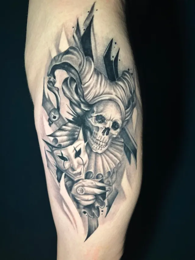Black and grey upper-arm tattoo of a jester skull with masks